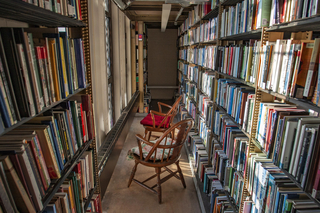 Two wooden chairs in an aisle between shelves of books in a library